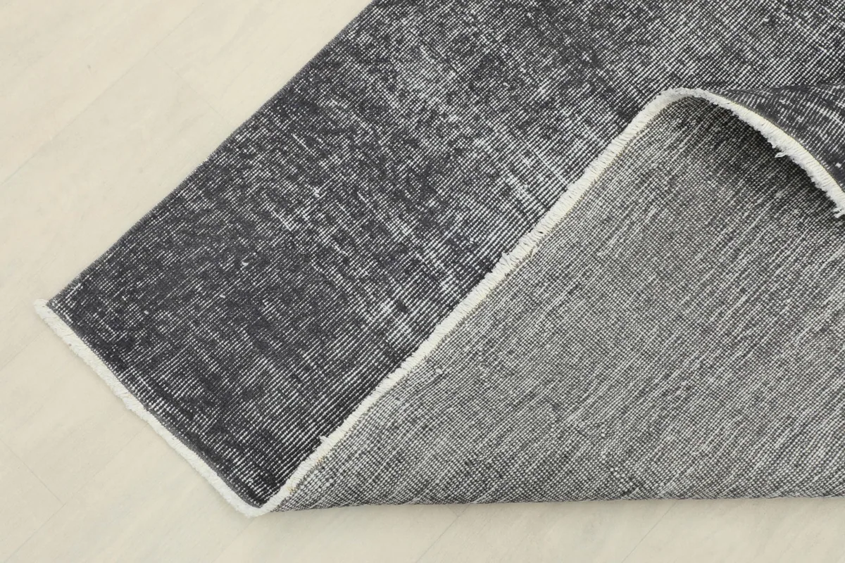 Corner of the rug folded back to show the cotton foundation and the reverse side of the hand-knotting.