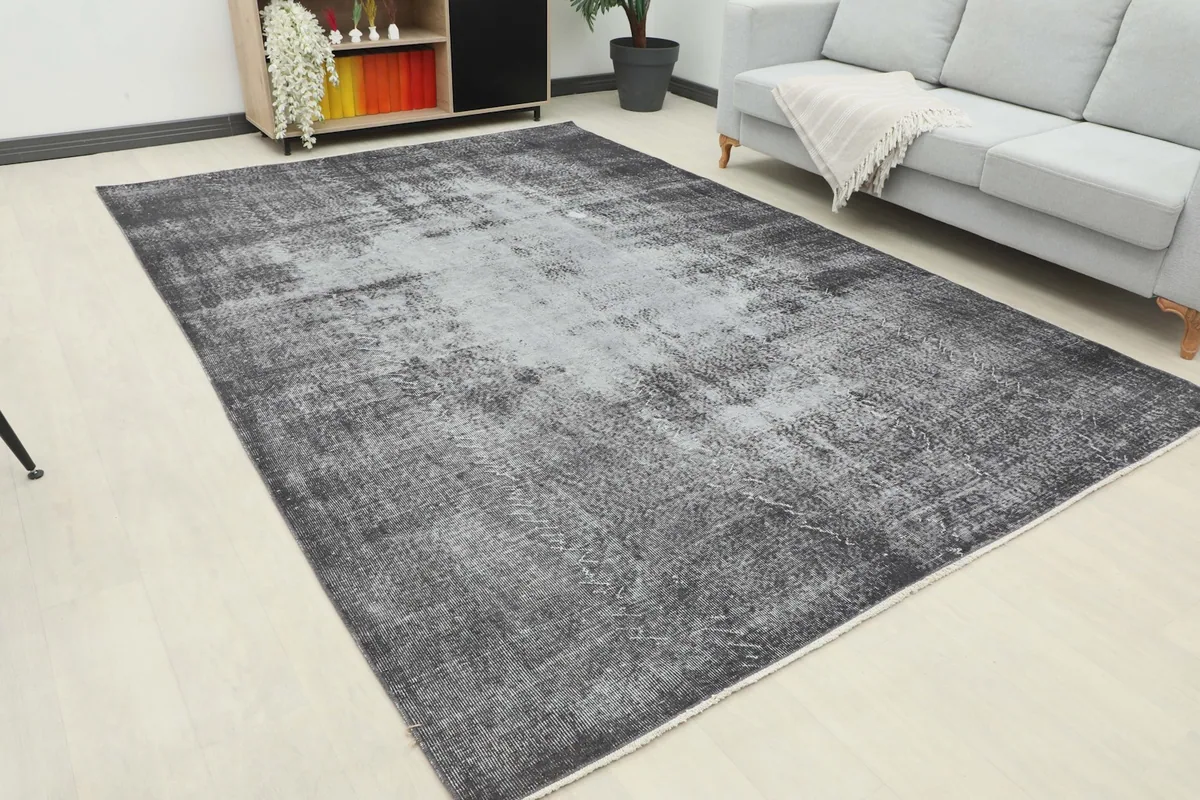 Angle view of the large charcoal and gray distressed rug placed under a light-colored sofa