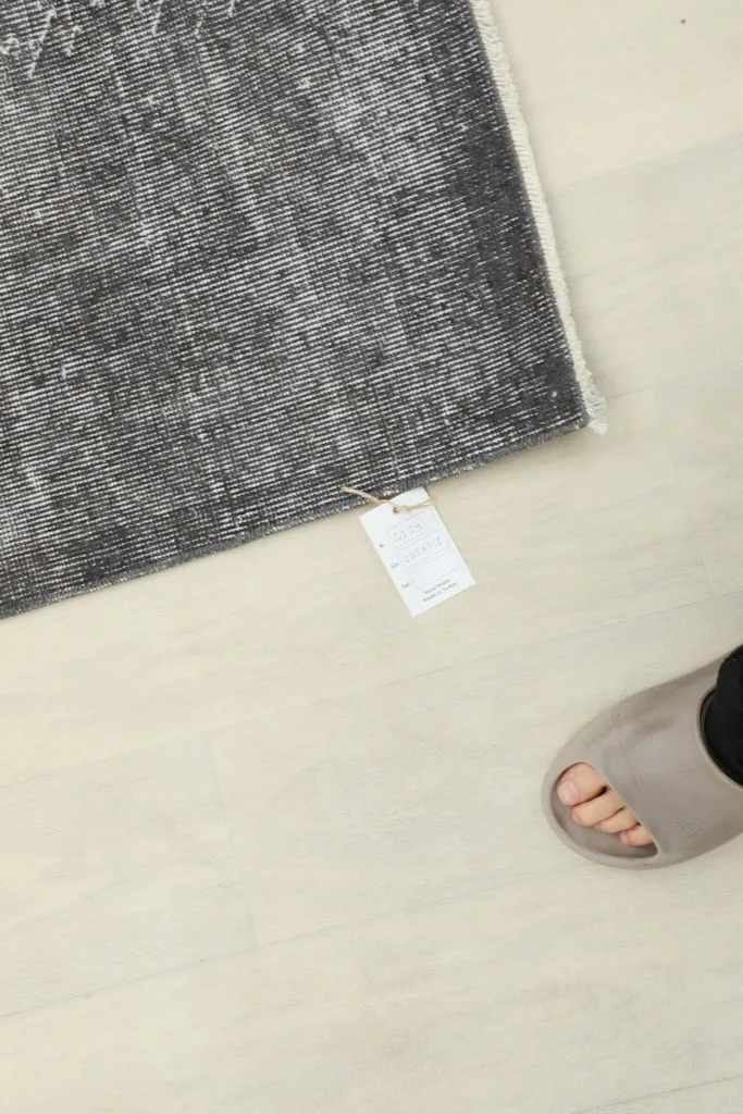 A person's foot next to the rug, indicating scale and showing the product tag