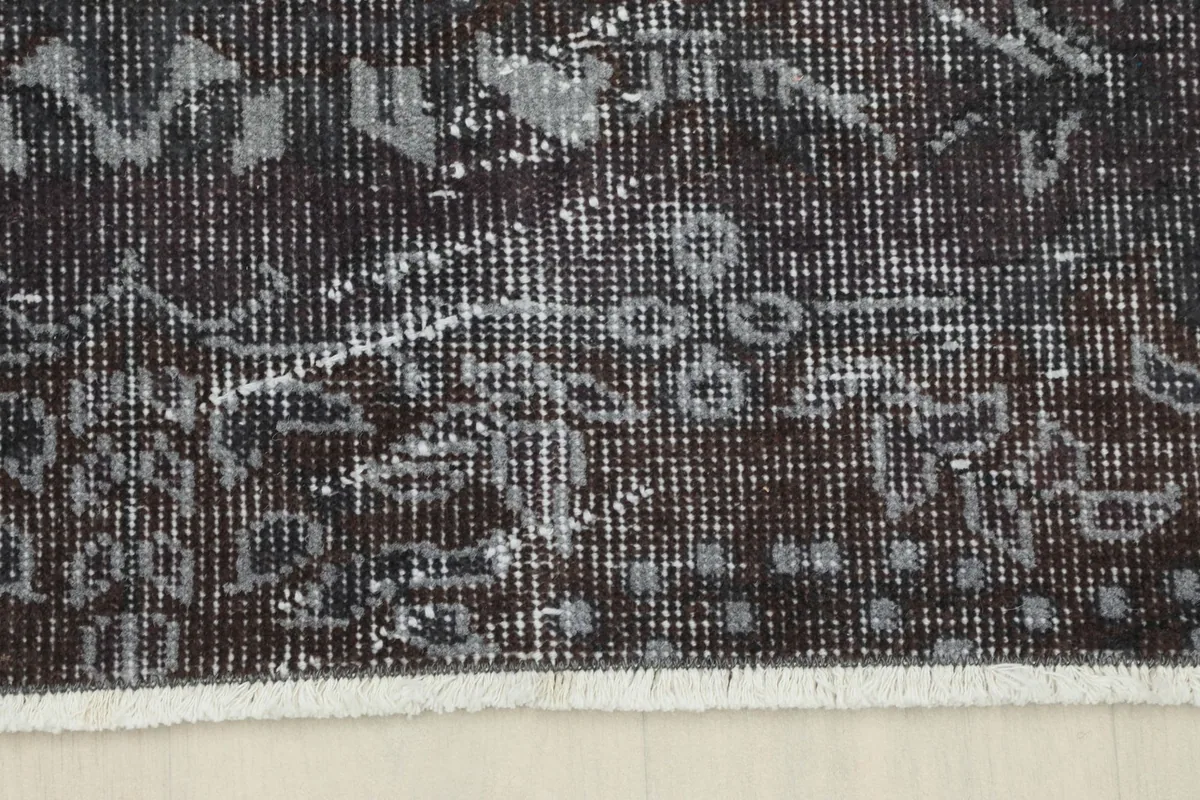 Edge of the charcoal rug with its border design and short, light-colored fringe