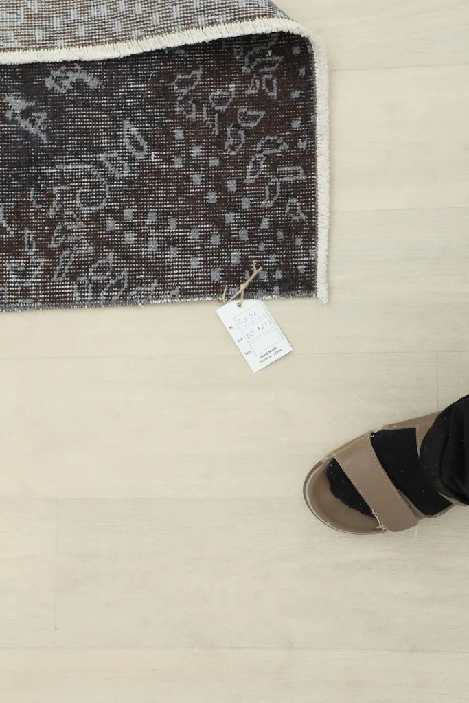 Overhead detail shot of the rug's corner with a product tag and a foot for scale