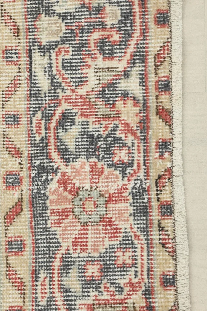 Close-up of the low wool pile and hand-knotted texture along the rug's edge, showing wear.