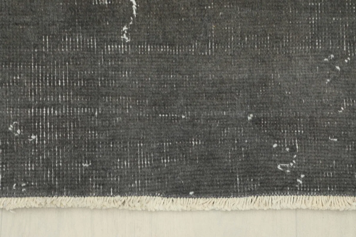 Edge of the charcoal rug showing the short, natural cotton fringe and border detail