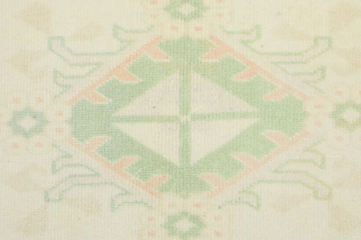 Macro detail of a green and rose geometric motif within the rug's pattern, showing individual knots.