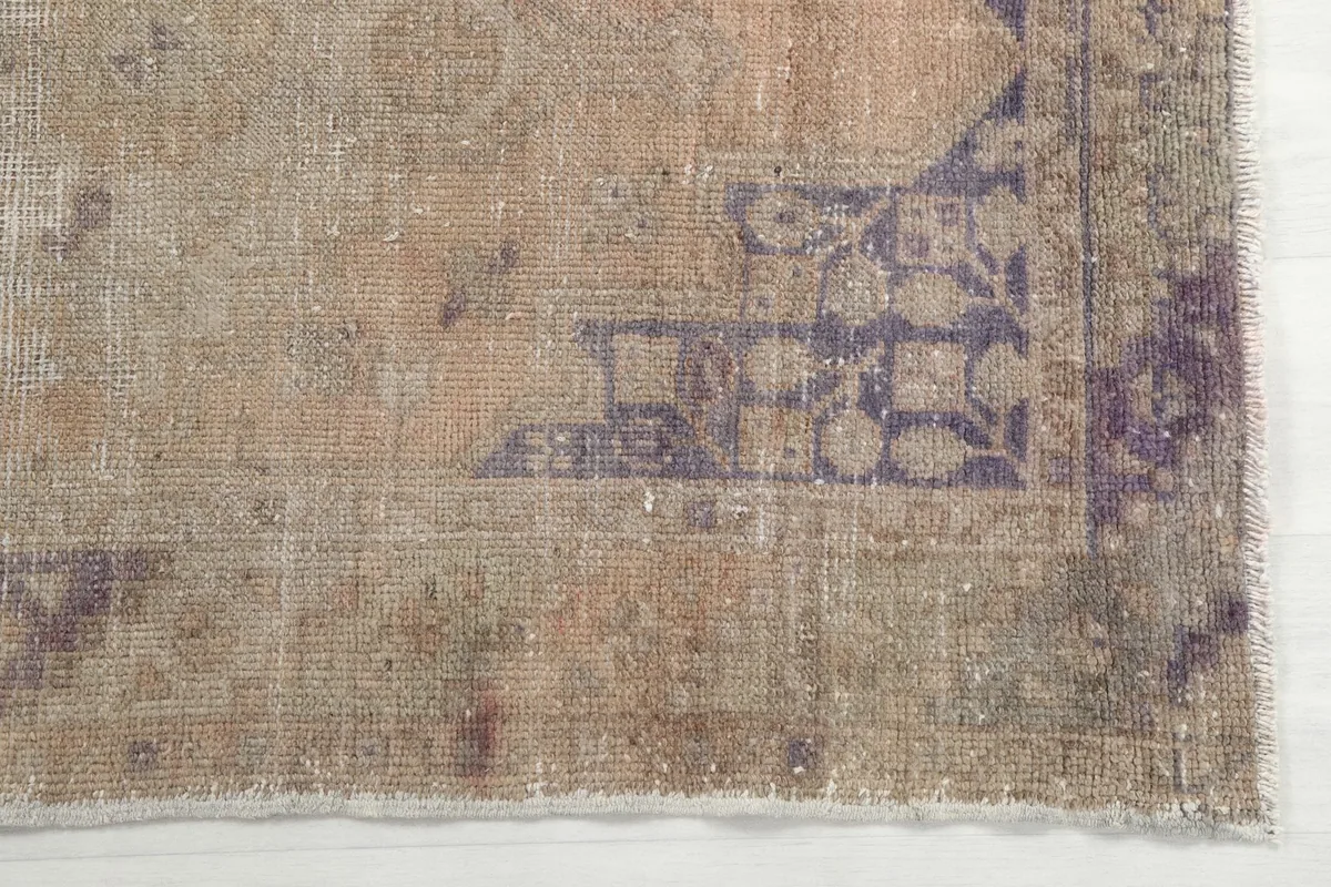 Detailed view of the purple geometric motifs and distressed beige pile at one end of the rug