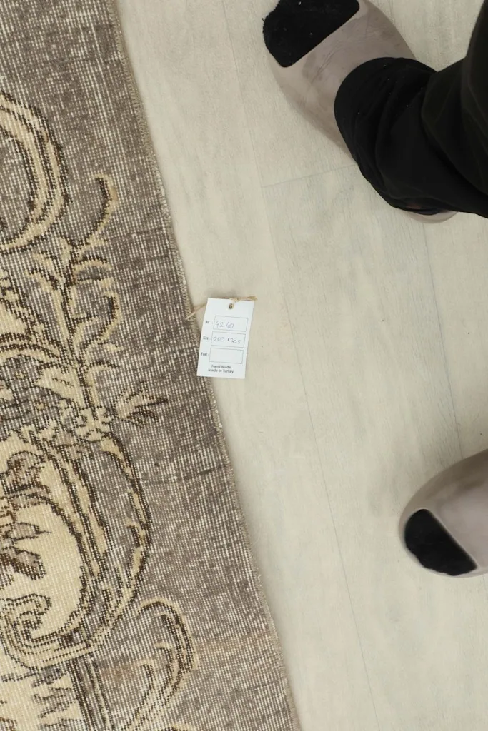 Overhead view of a person's feet near the rug, with a product tag visible on the floor next to it.