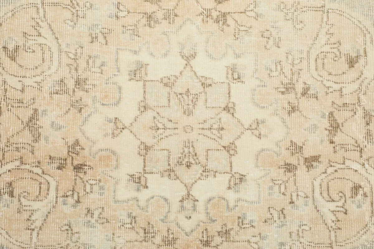 Detailed view of the beige floral motifs and faded colors on the vintage wool pile