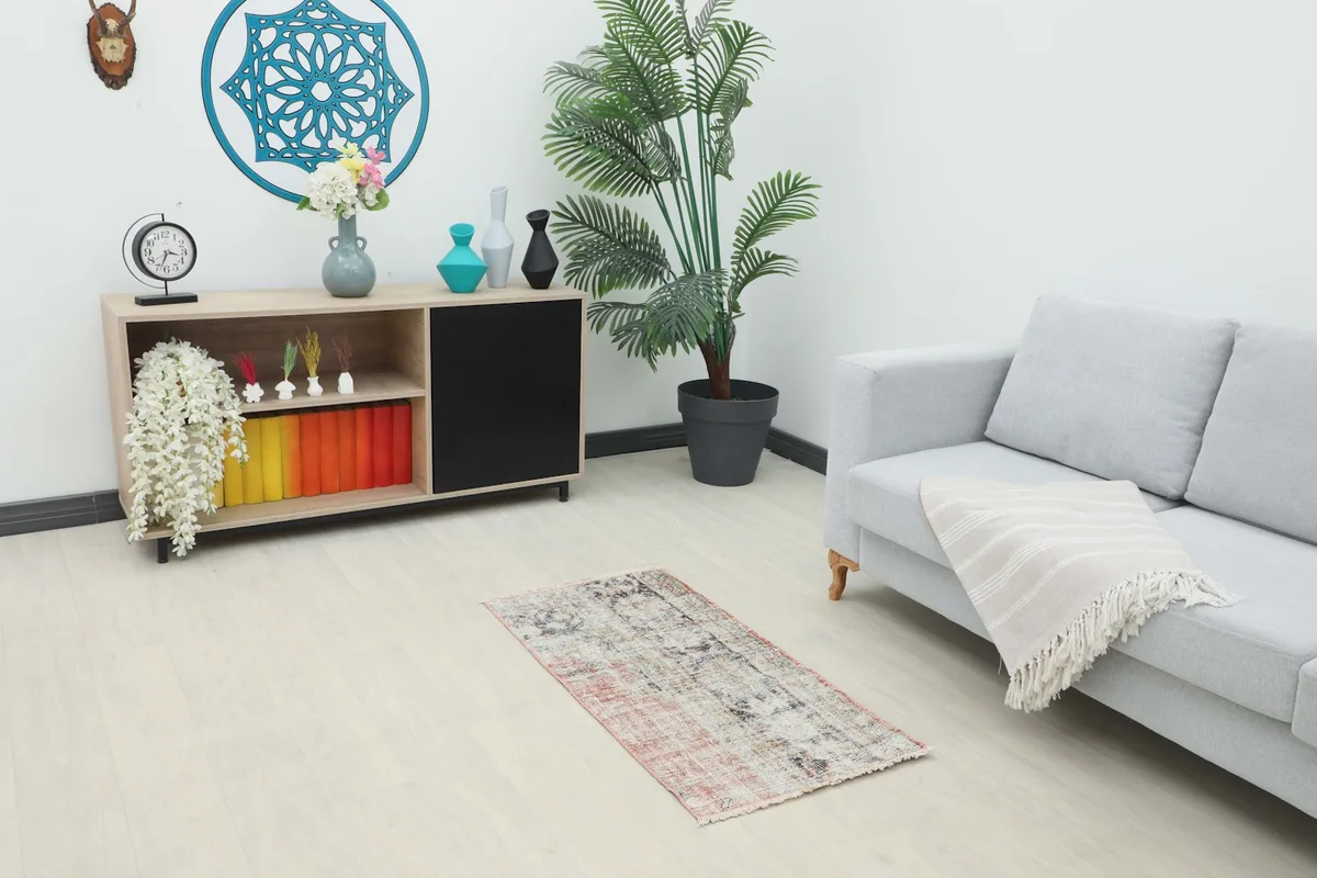 Vintage Anatolian rug placed in a living room setting, next to a sofa and cabinet, showing its scale.