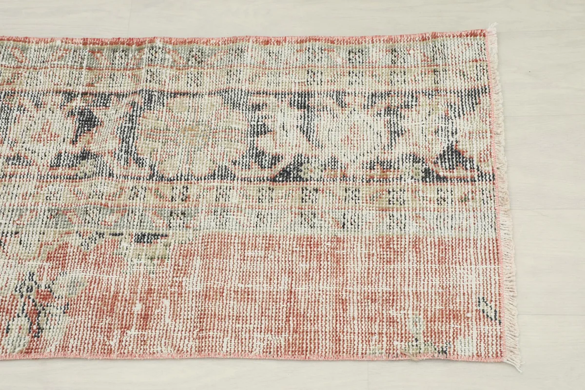 Close-up view of one end of the rug, showing the faded rust field and intricate geometric patterns.