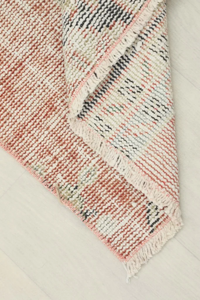 View of the rug's corner folded back, revealing the reverse side and the hand-knotted construction.