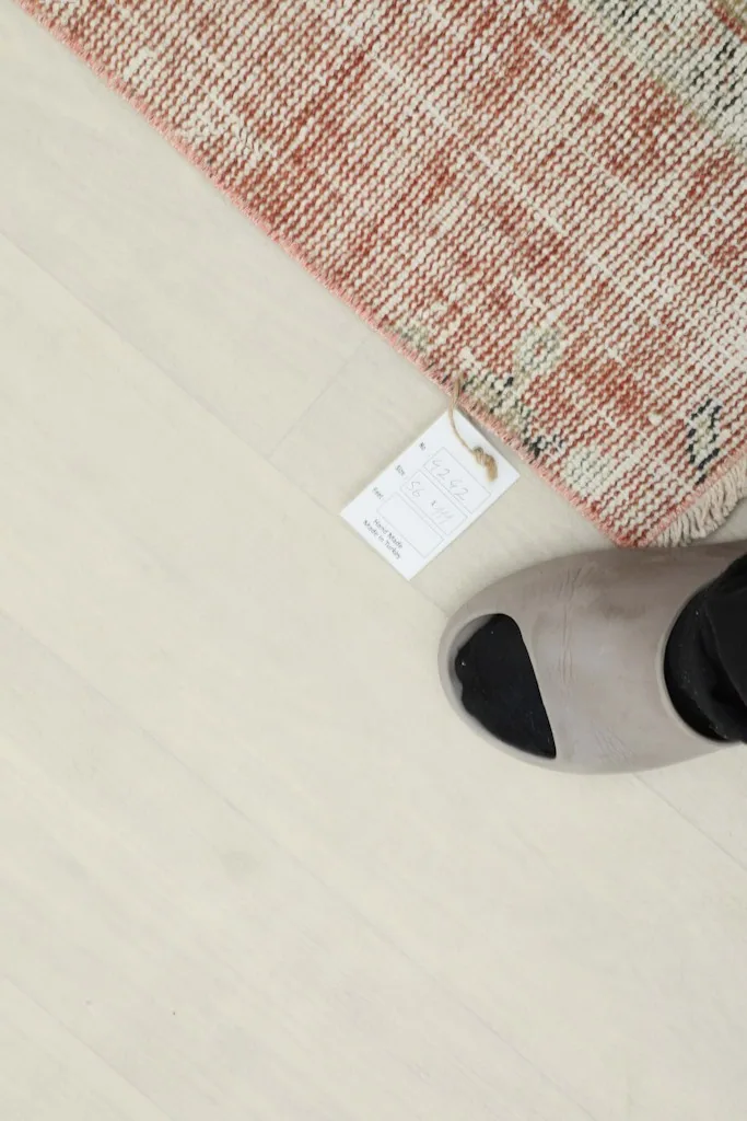 A foot next to the rug, showing its small scale and placement on a light wood floor.