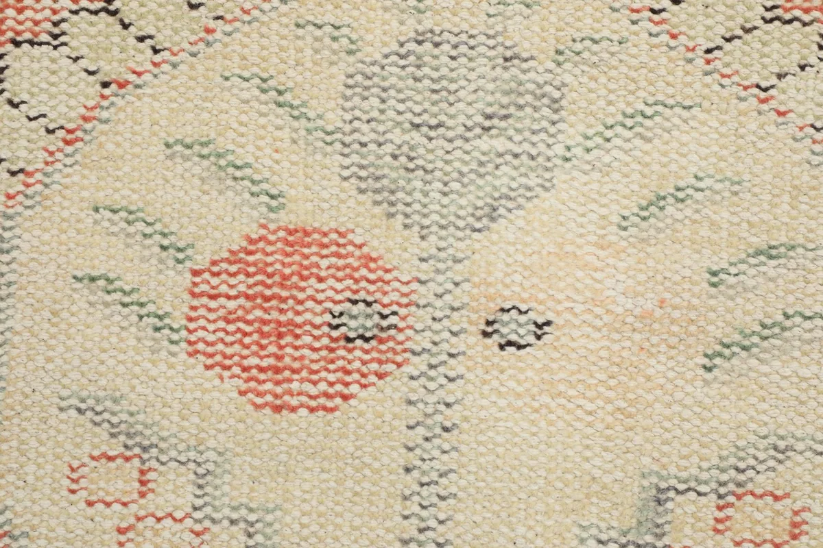 Macro detail of the hand-knotted wool pile, showing the red, gray, and green threads in the ivory medallion.