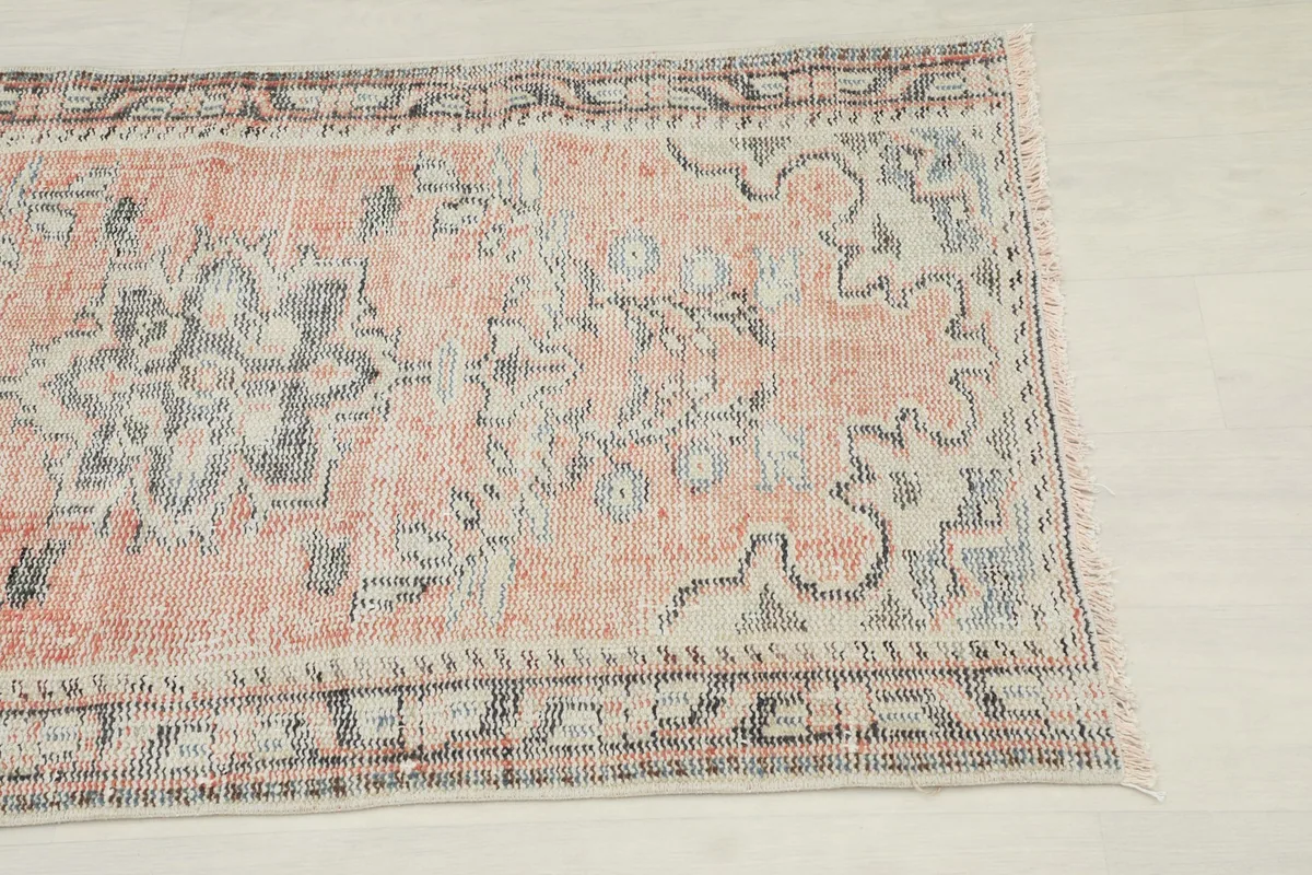 Close-up detail of the vintage rug's upper right section, showing faded orange and gray motifs.