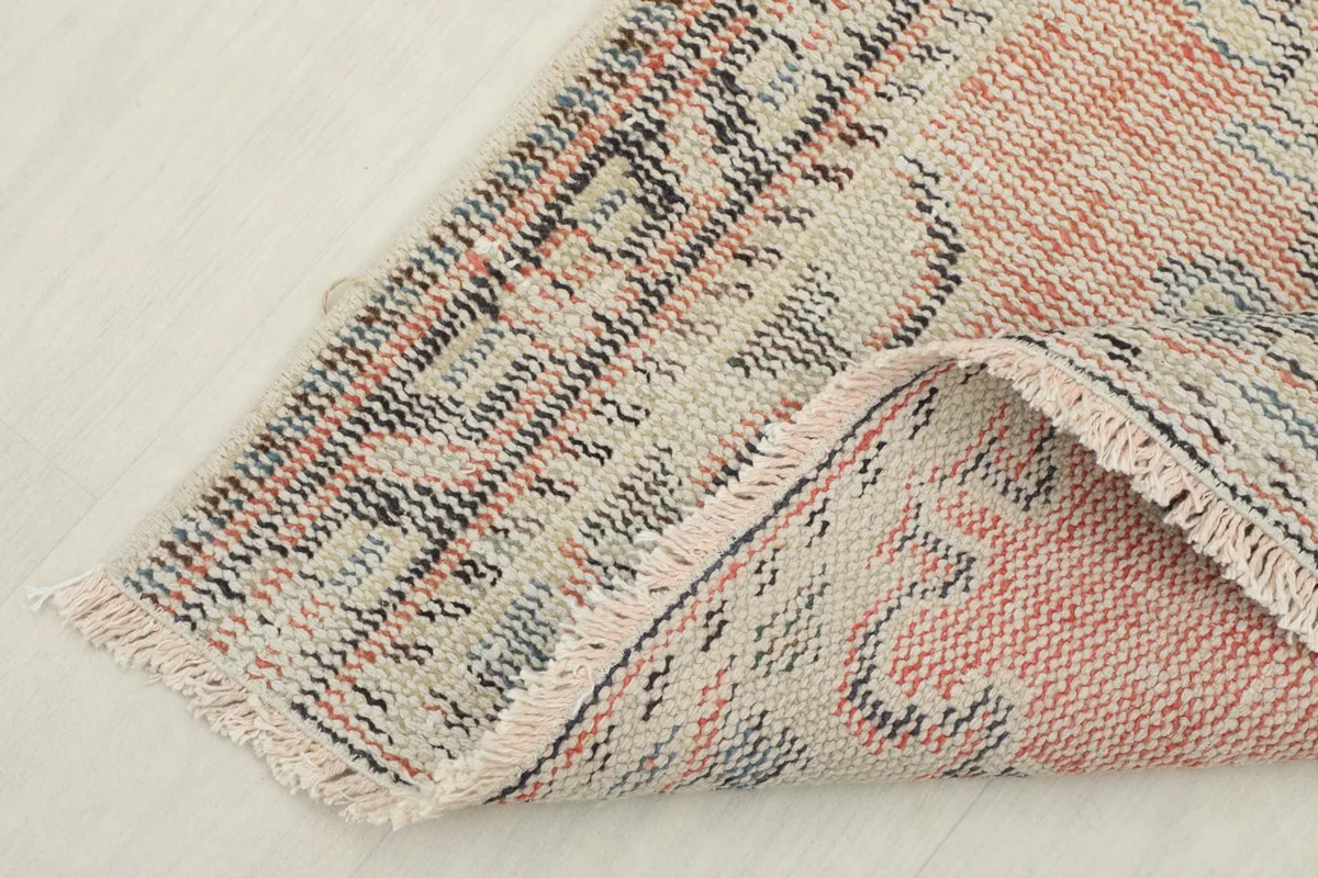 Corner of the vintage rug folded back to show the cotton foundation and the reverse side.