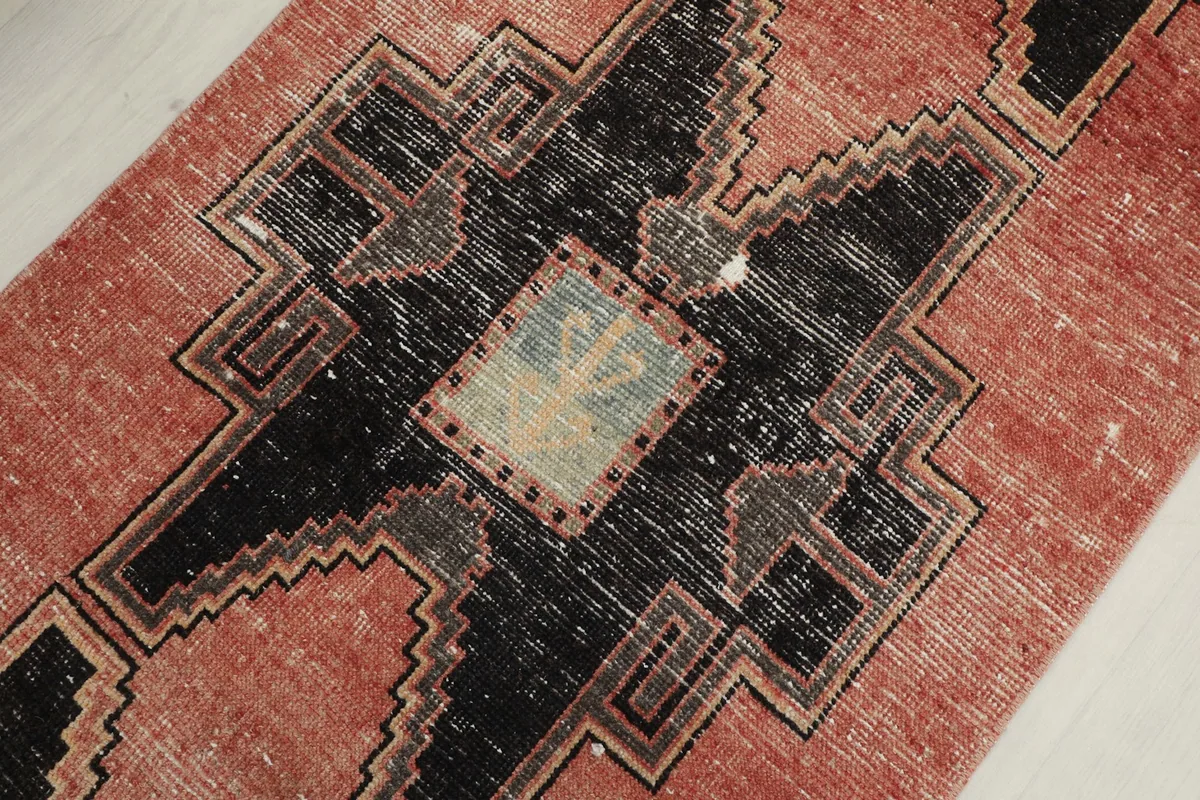 Detailed view of a central black geometric motif with faded rose, olive, and blue elements within the pattern.