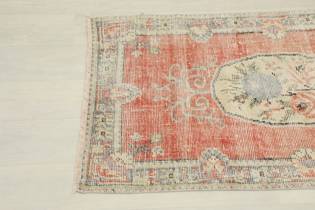 Close-up view of the lower left corner of the rug, showing the faded rust field and blue border