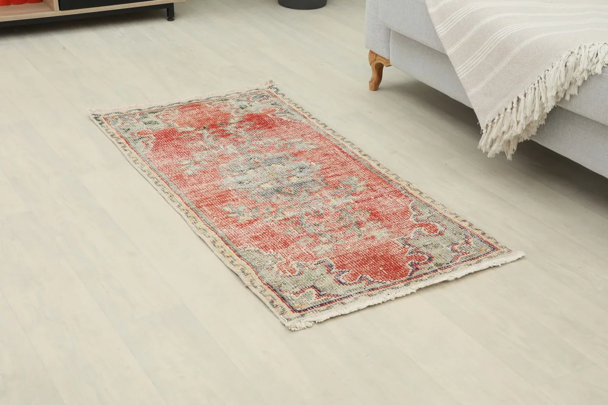 Angled view of the vintage red rug on a light floor, showing its placement relative to a sofa.