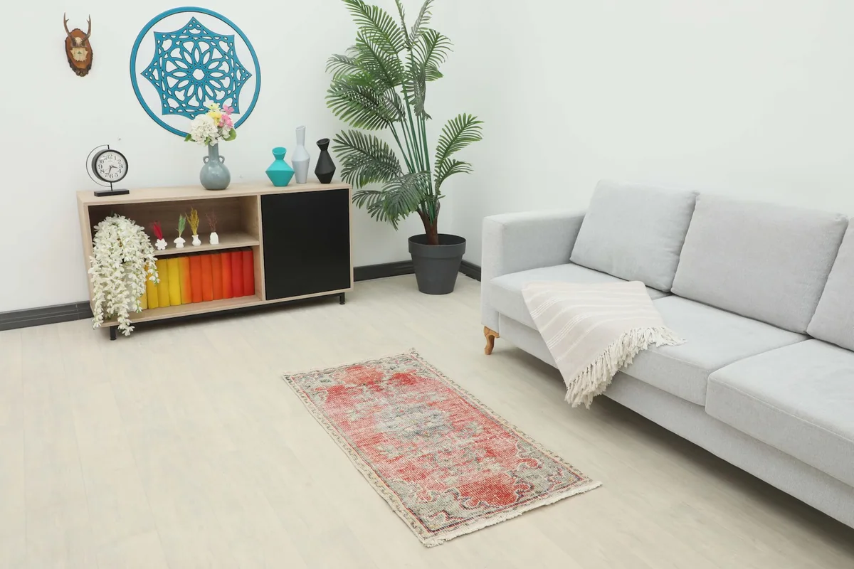 Vintage red area rug placed in a modern living room setting with a gray sofa and wooden cabinet.