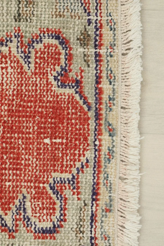 Close-up of the rug's short, natural ivory fringe and the edge of the red and gray border.