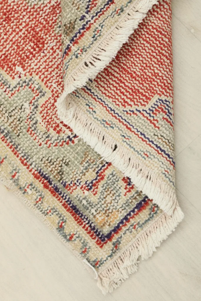 Corner of the rug folded back, revealing the backside of the hand-knotted cotton foundation.