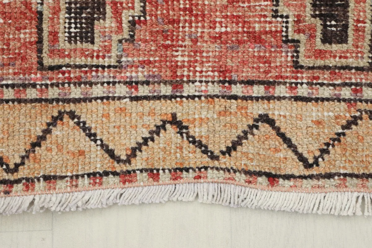 Close-up of the rug's end, showing the tan border with a zigzag pattern and short fringes.