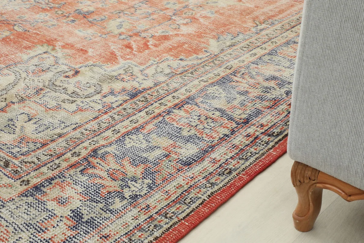 Detail of the rug's navy and cream patterned border next to a couch leg, showing color variation.