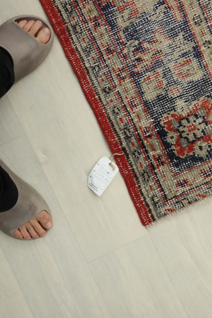 Top-down view of a corner of the rug, showing the wool pile and a size tag near feet.