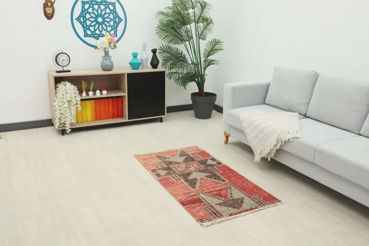 Red tribal rug displayed in a modern living room setting with a gray sofa and wooden cabinet