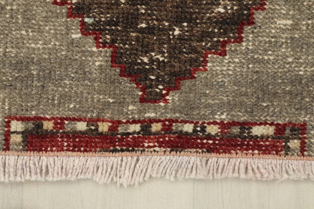 Close-up of the rug's short, light-colored fringe and the edge of the red and gray pattern