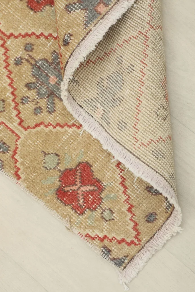 Corner of the rug folded back, revealing the cotton foundation and reverse side of the knots.
