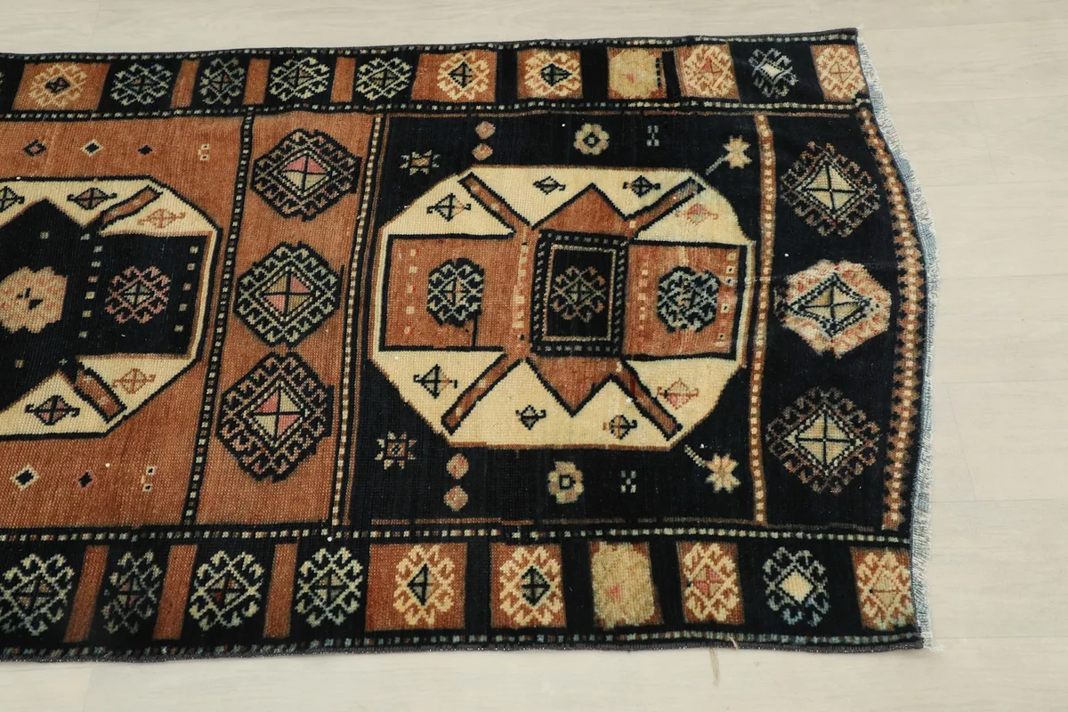 Close-up of one end of the rug, highlighting the black field, rust border, and geometric patterns.