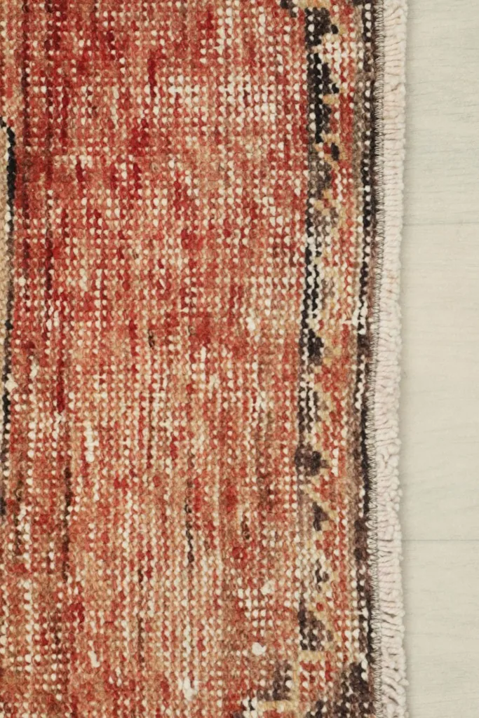 Close-up of the rug's side border and short fringe, showing the weave and distressed areas.