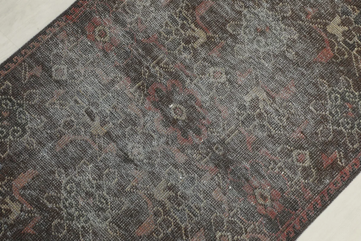 Overhead view focusing on the faded central field of the charcoal and red vintage runner.