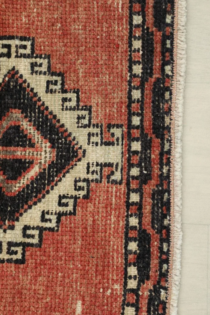 Edge detail of the rust runner rug, showing the black and beige border design