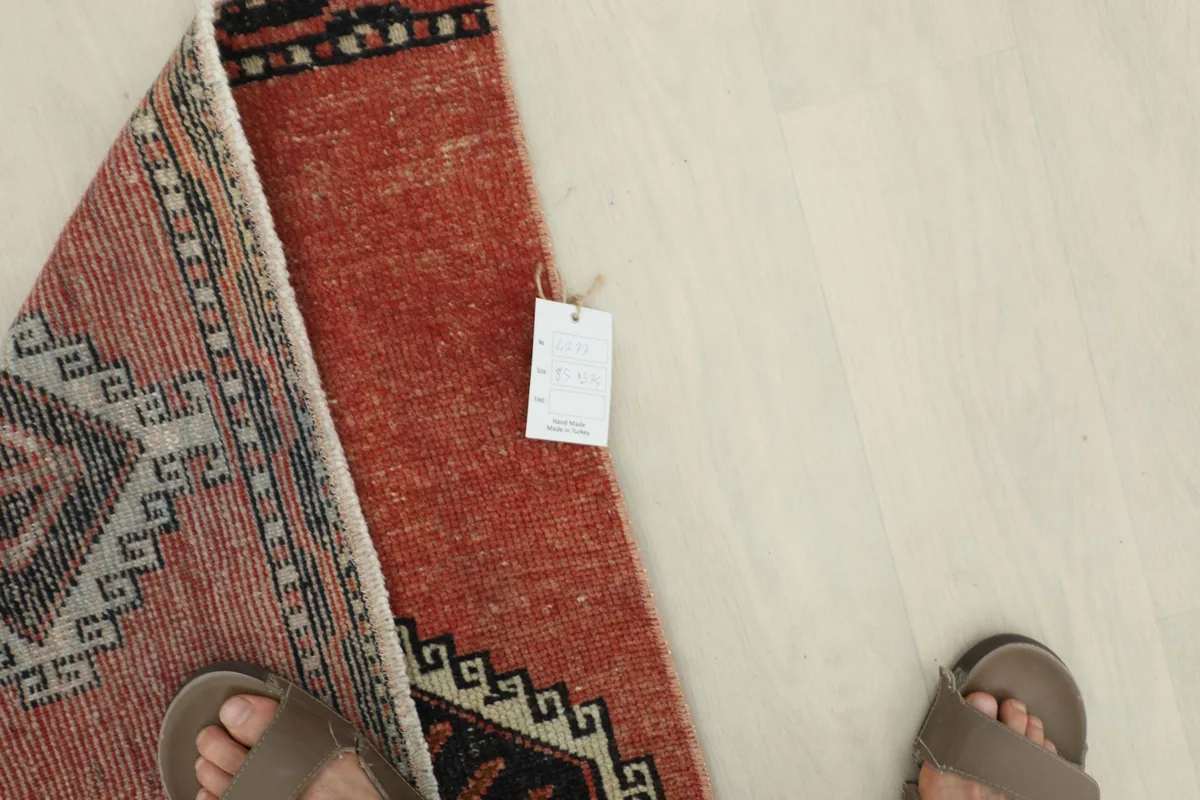 Overhead view of a section of the rust runner rug with a tag and feet for scale