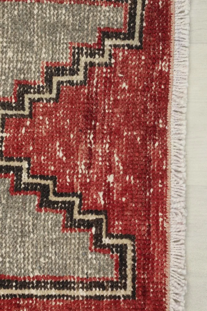 Close-up of the short white fringe and the edge of the red and gray geometric runner.