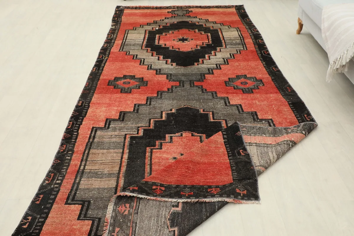 Angled view of the full rug with one end slightly folded, showcasing the red, gray, and black design.