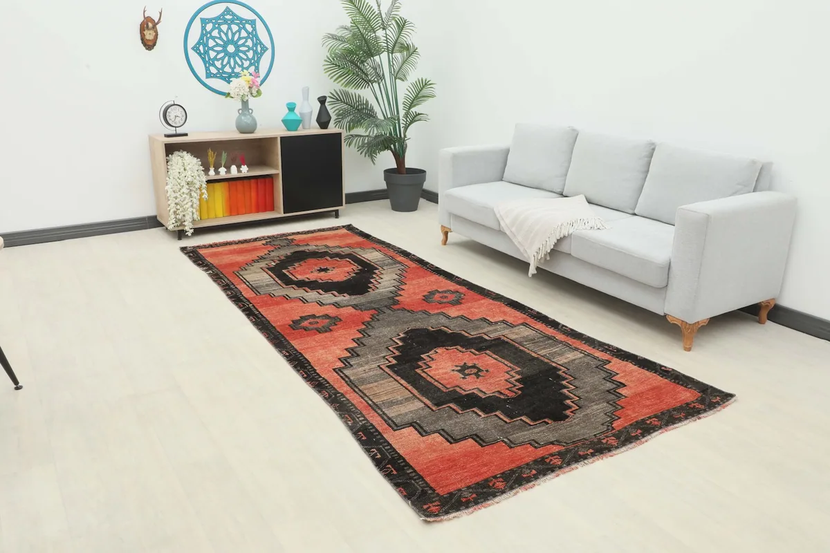 Vintage Anatolian area rug with red, gray, and black geometric patterns placed in a modern living room setting.