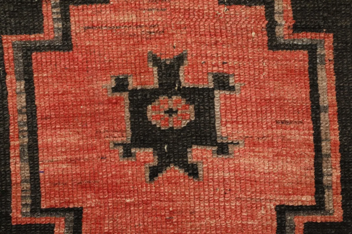 Close-up of a small stylized black motif on the red field, surrounded by gray and black geometric lines.