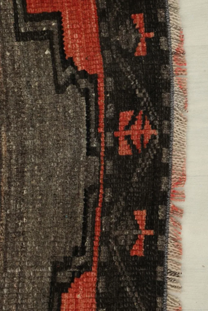 Detailed view of the rug's black border with small red geometric patterns and the woven edge.