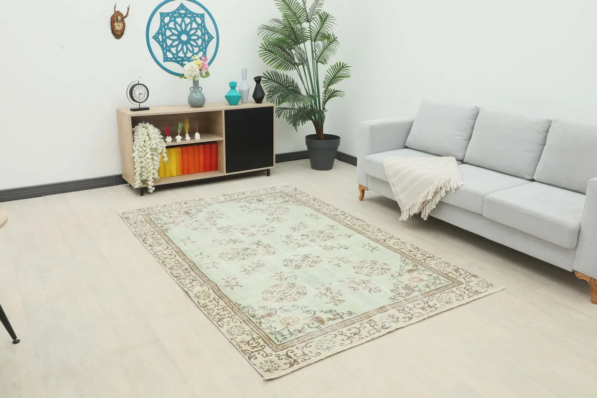 Vintage Anatolian rug with soft green field and floral motifs placed in a modern living room setting.