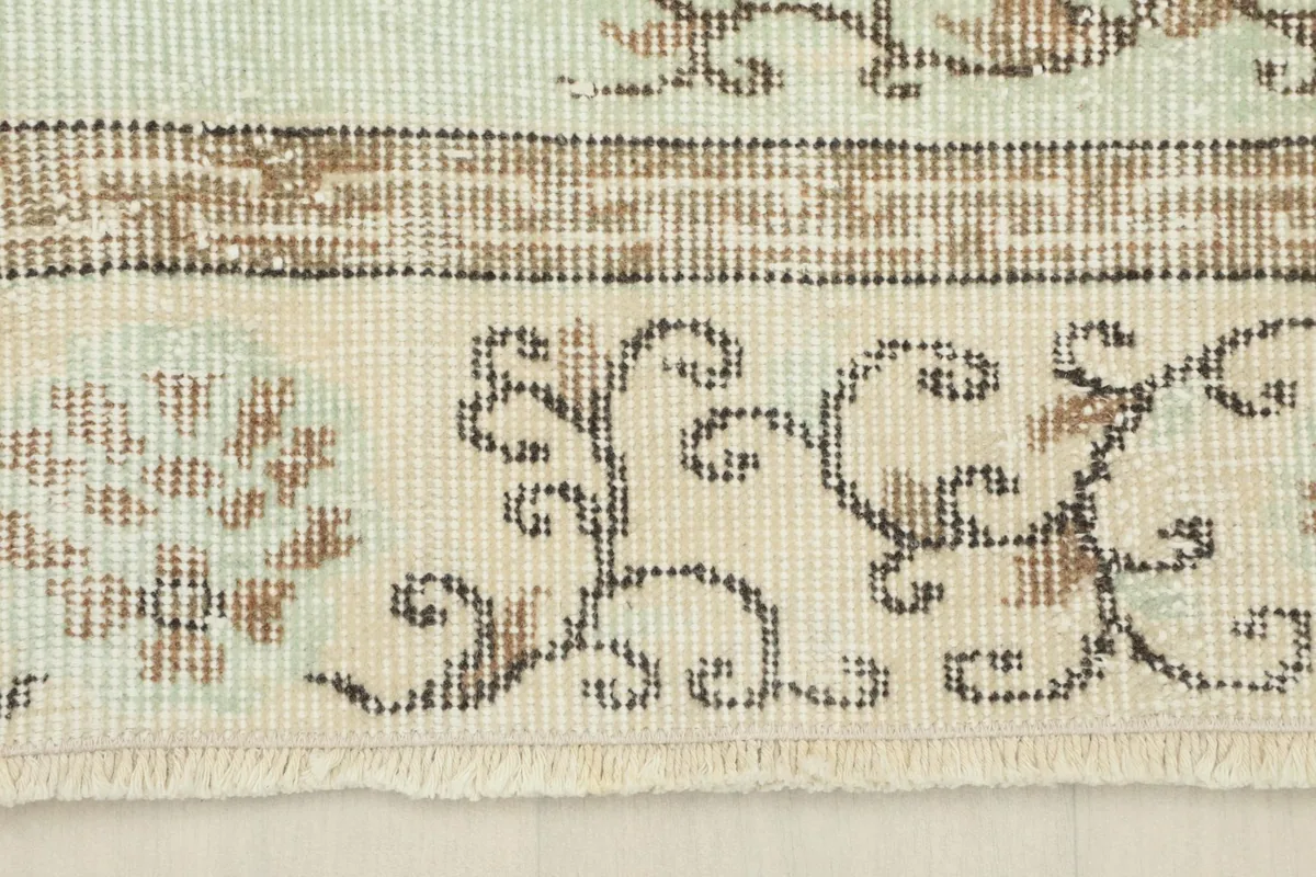 Detailed shot of the rug's beige border with brown scrollwork and the short, hand-finished fringe.