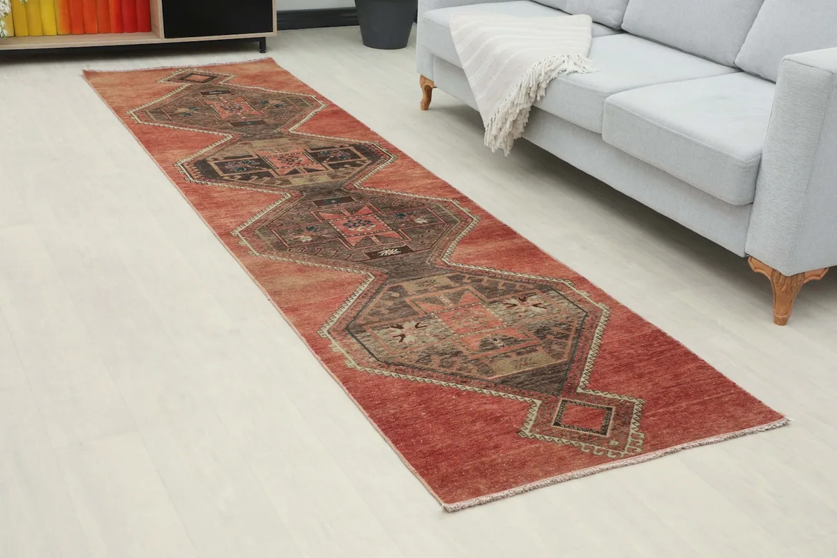 Angled view of the runner rug in a room, highlighting the rust field and tribal patterns