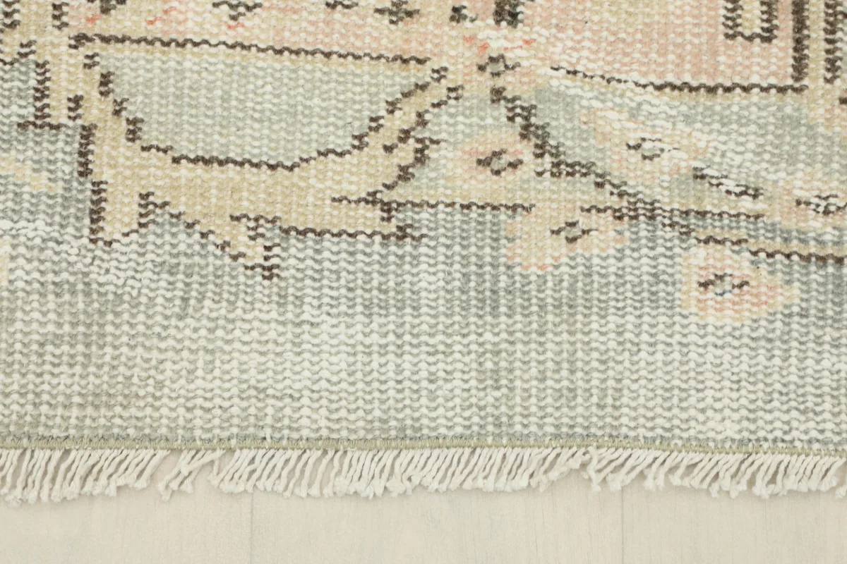 Detail of the Faded Gray Rose Medallion Rug's fringe and the edge of the cotton foundation.