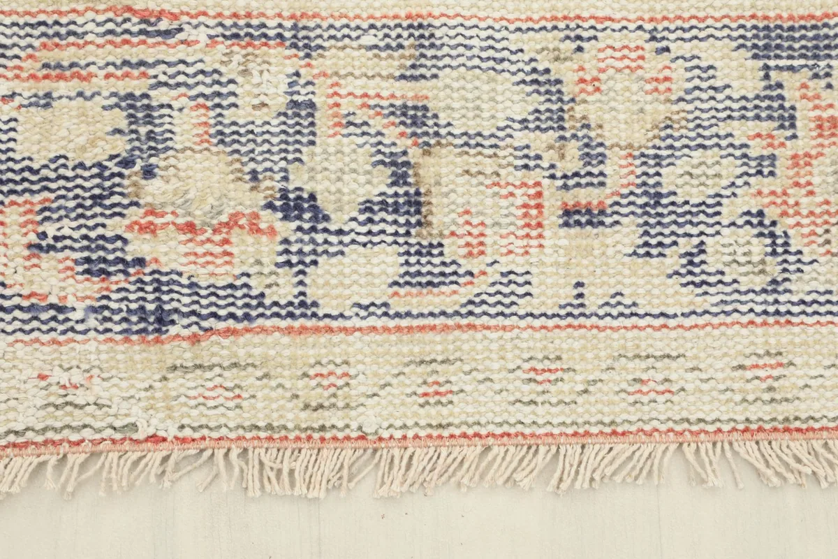 Detail of the rug's fringe and the edge of the navy and rust patterned border