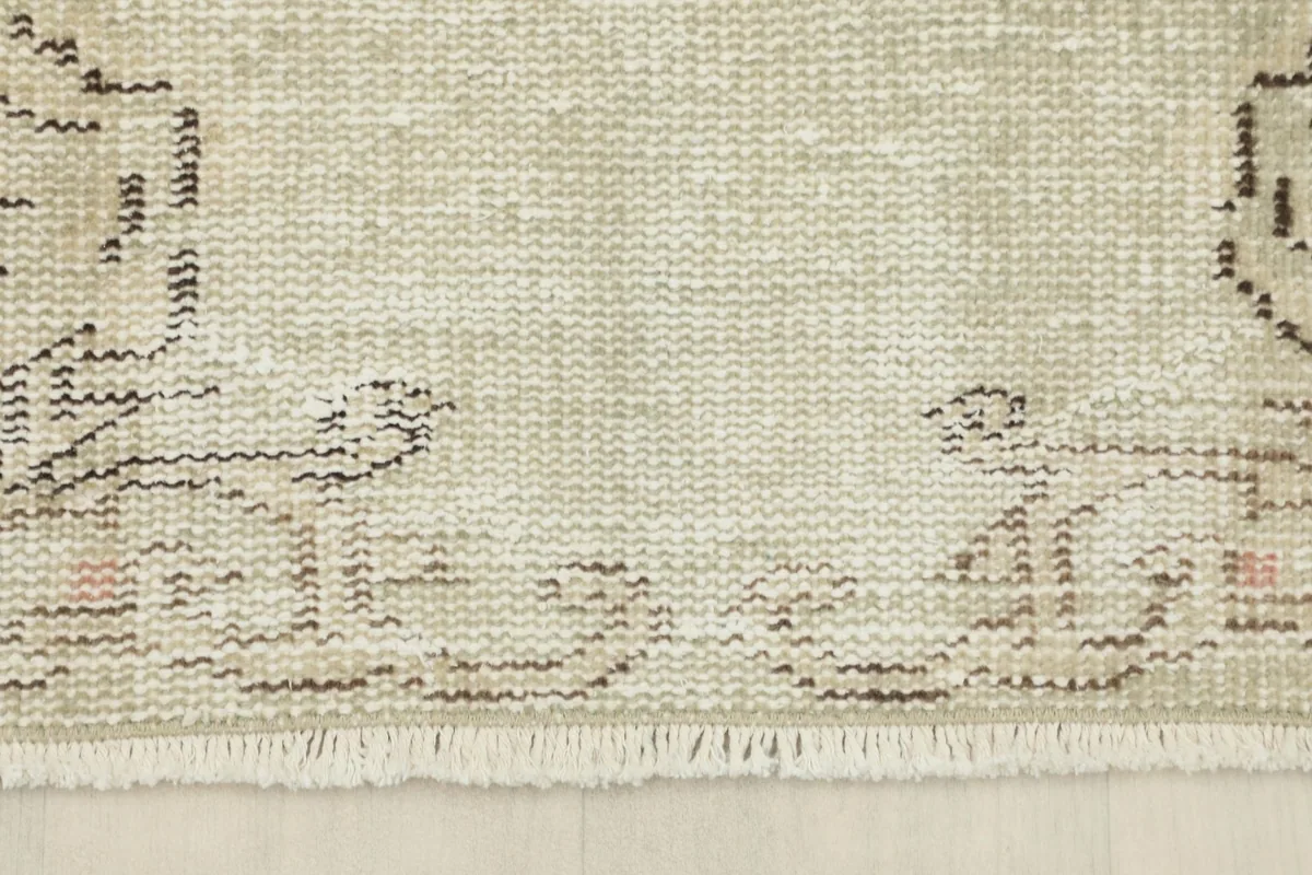 Close-up of the rug's short, light-colored fringe and the edge of the hand-knotted construction