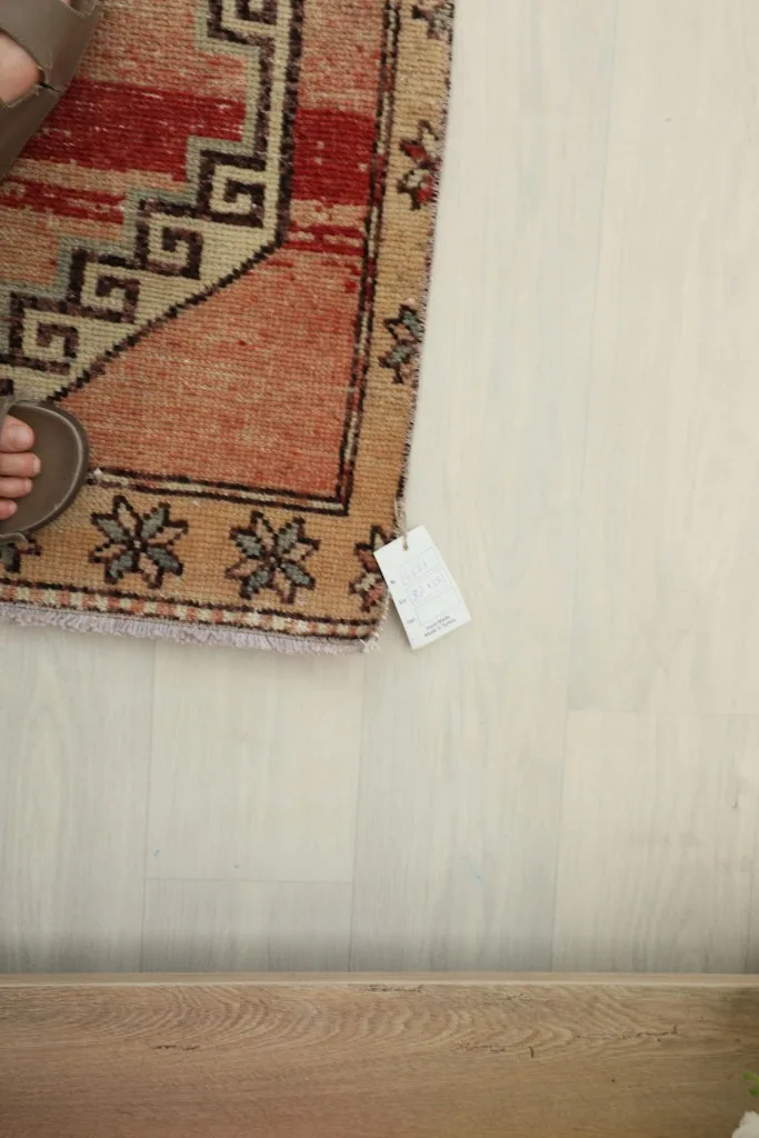 Corner of the rug with a size tag and a foot for scale, highlighting the fringe