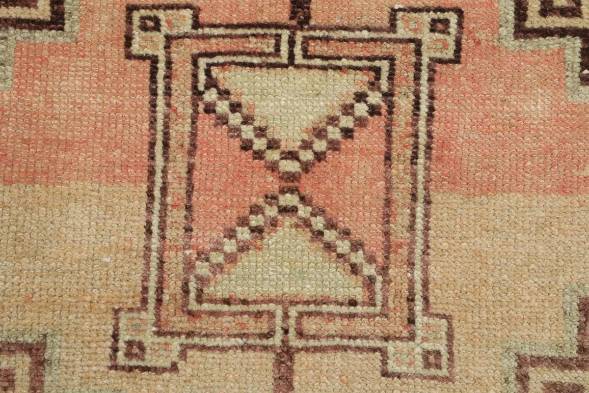 Extreme close-up of a central geometric element, revealing the knotting and color variations in pink and beige