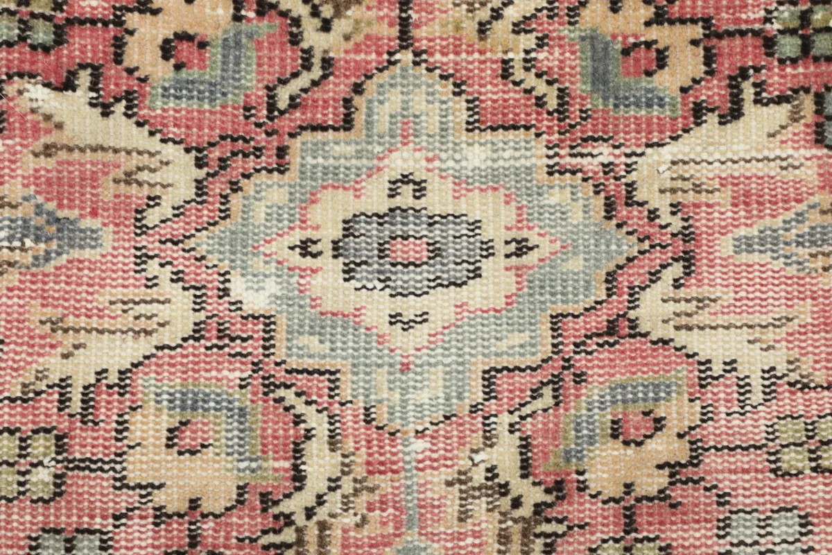 Close-up of a central medallion detail showing individual knots and color variations in rose, gray, and beige