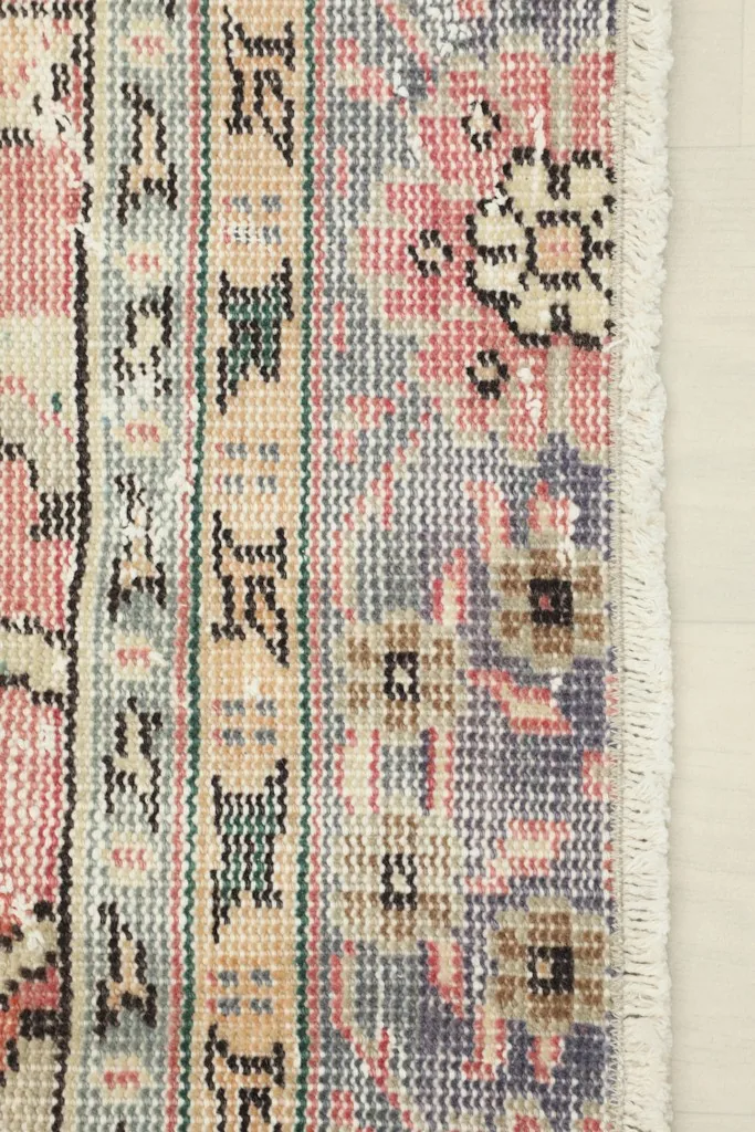 Close-up of the rug's border design with gray, beige, and rose elements, and the short fringe